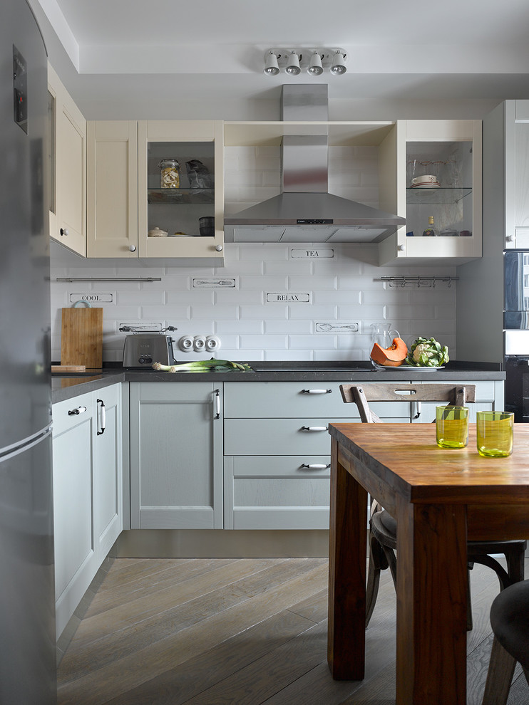 Modern inredning av ett grå grått l-kök, med skåp i shakerstil, grå skåp, vitt stänkskydd, stänkskydd i tunnelbanekakel, svarta vitvaror och brunt golv