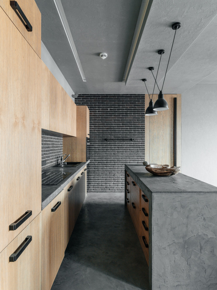 Bild på ett industriellt grå grått parallellkök, med en nedsänkt diskho, släta luckor, skåp i ljust trä, grått stänkskydd, stänkskydd i tegel, betonggolv, en köksö och grått golv