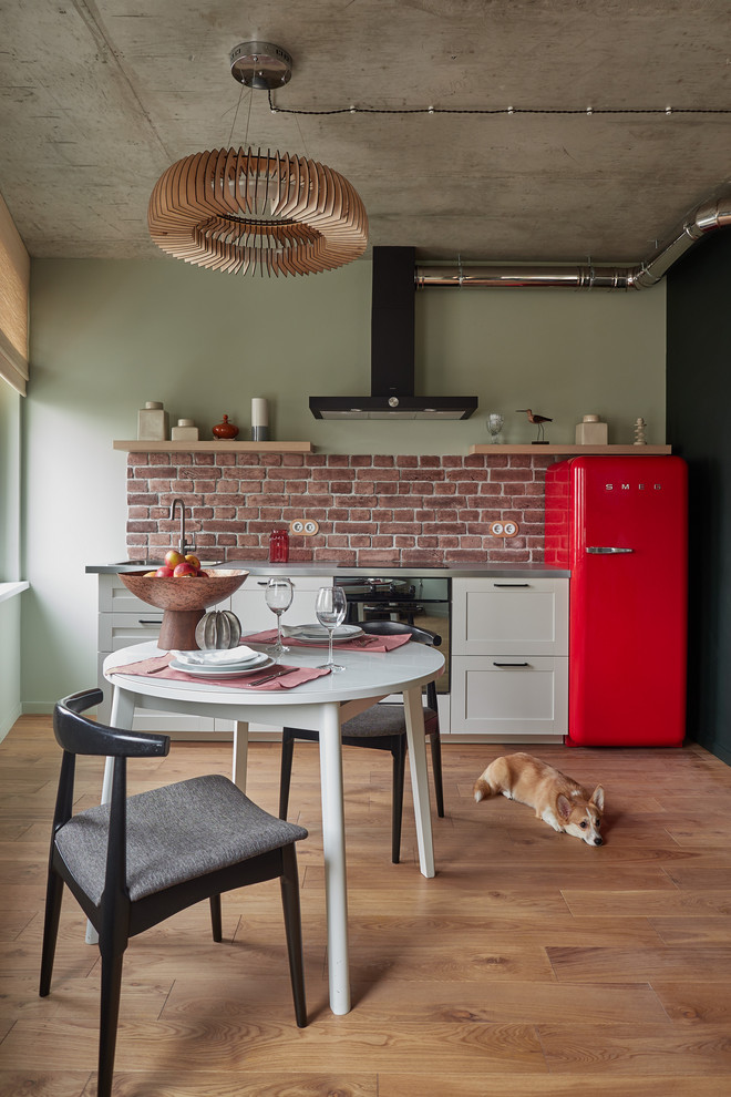 Immagine di una piccola cucina abitabile industriale con lavello integrato, ante in stile shaker, ante bianche, top in acciaio inossidabile, paraspruzzi rosso, paraspruzzi in mattoni, elettrodomestici colorati e parquet chiaro