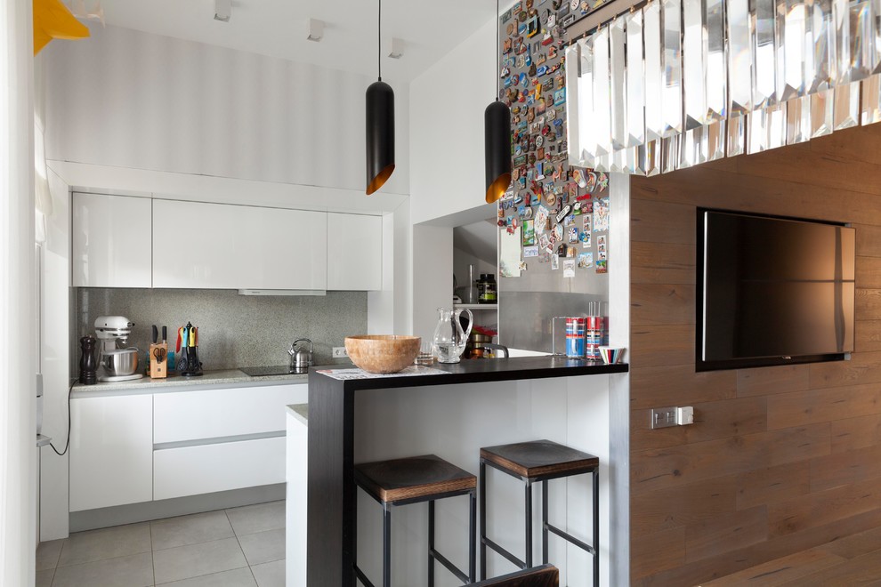 На фото: параллельная кухня в современном стиле с плоскими фасадами, белыми фасадами, серым фартуком, полуостровом, серым полом и серой столешницей
