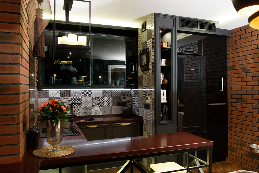 На фото: п-образная кухня-гостиная в стиле лофт с врезной мойкой, плоскими фасадами, черными фасадами, полуостровом и разноцветным фартуком с
