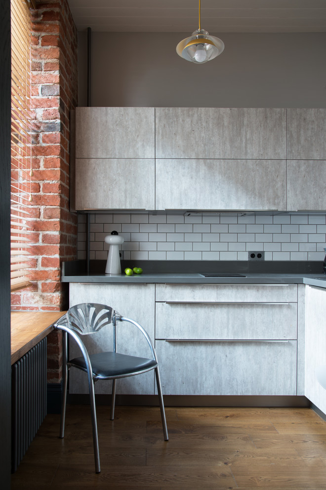 Bild på ett litet industriellt grå grått l-kök, med släta luckor, grå skåp och vitt stänkskydd