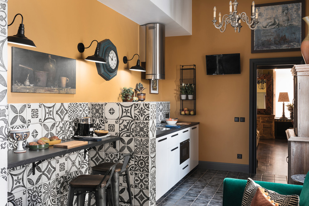 Immagine di una piccola cucina mediterranea con pavimento con piastrelle in ceramica, pavimento grigio, lavello da incasso, ante lisce, ante bianche, paraspruzzi multicolore, elettrodomestici neri, nessuna isola e top nero