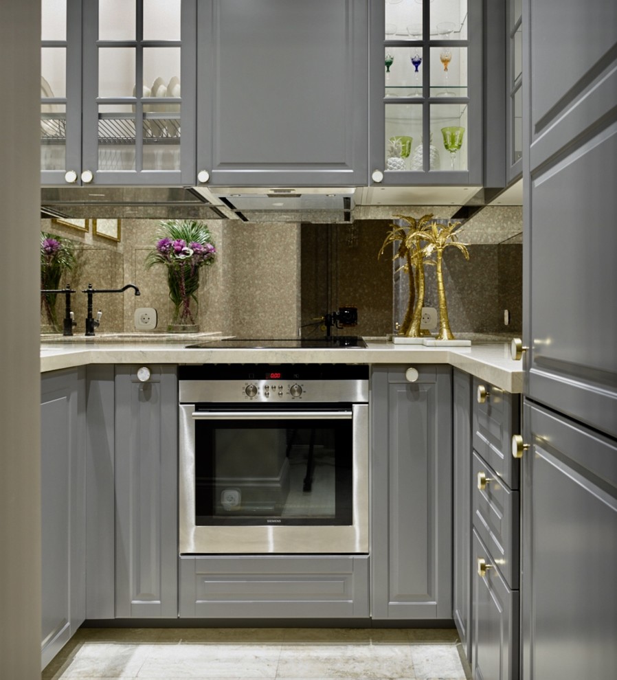 Immagine di una piccola cucina ad U chic con ante grigie, elettrodomestici in acciaio inossidabile, pavimento beige, ante di vetro, paraspruzzi a specchio e top beige
