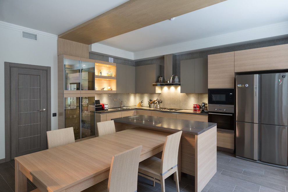 Example of a trendy l-shaped gray floor eat-in kitchen design in Other with flat-panel cabinets, light wood cabinets, gray backsplash, stainless steel appliances and an island