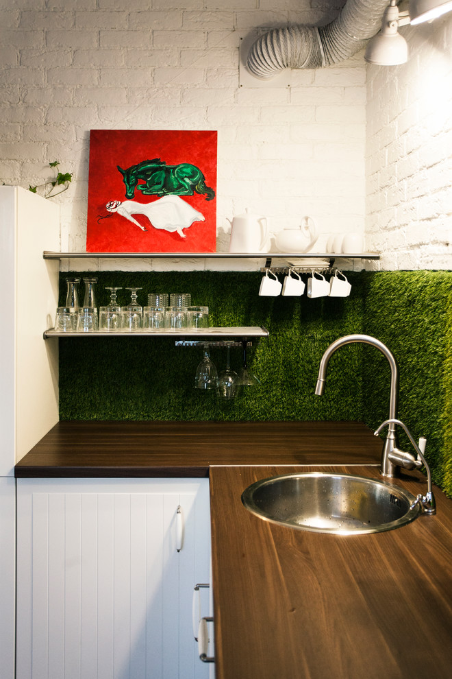 На фото: маленькая угловая кухня в современном стиле с накладной мойкой, деревянной столешницей, зеленым фартуком и белыми фасадами для на участке и в саду