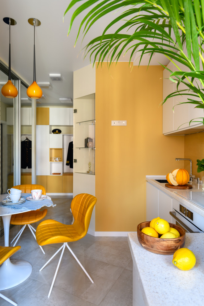 This is an example of a small contemporary l-shaped enclosed kitchen in Moscow with a submerged sink, white cabinets, composite countertops, yellow splashback, white appliances, porcelain flooring, no island, grey floors and white worktops.