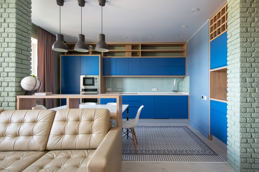 This is an example of a contemporary single-wall open plan kitchen in London with flat-panel cabinets, blue cabinets, white splashback, glass sheet splashback and stainless steel appliances.