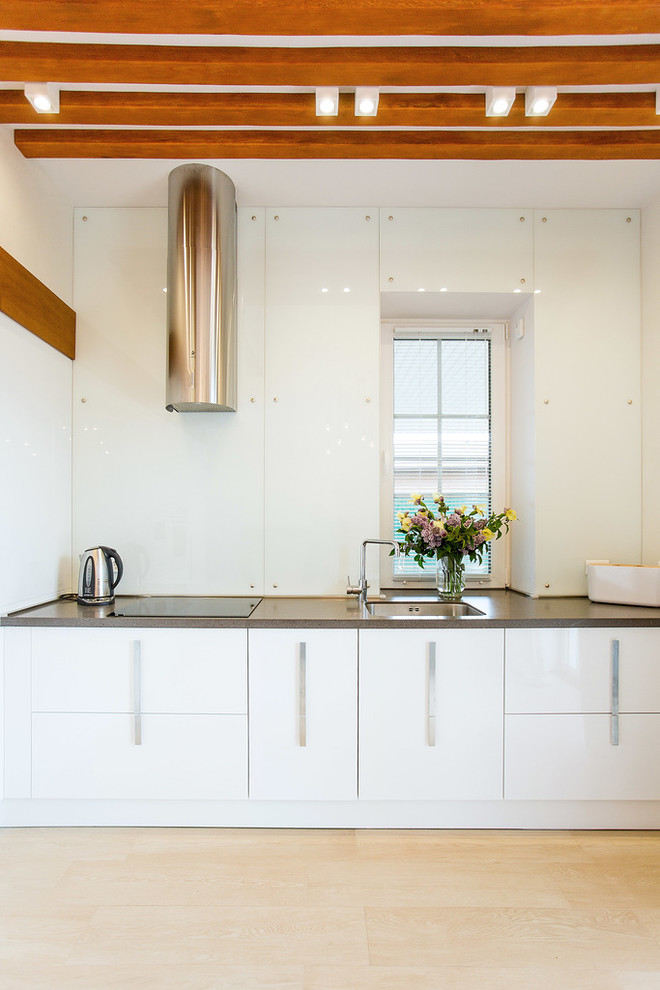 Einzeilige Moderne Küche mit Unterbauwaschbecken, flächenbündigen Schrankfronten, weißen Schränken, Küchenrückwand in Weiß, Glasrückwand und hellem Holzboden in Sonstige