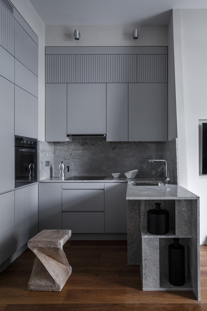 Idéer för funkis grått u-kök, med en undermonterad diskho, släta luckor, grå skåp, grått stänkskydd, svarta vitvaror, mellanmörkt trägolv, en halv köksö och brunt golv