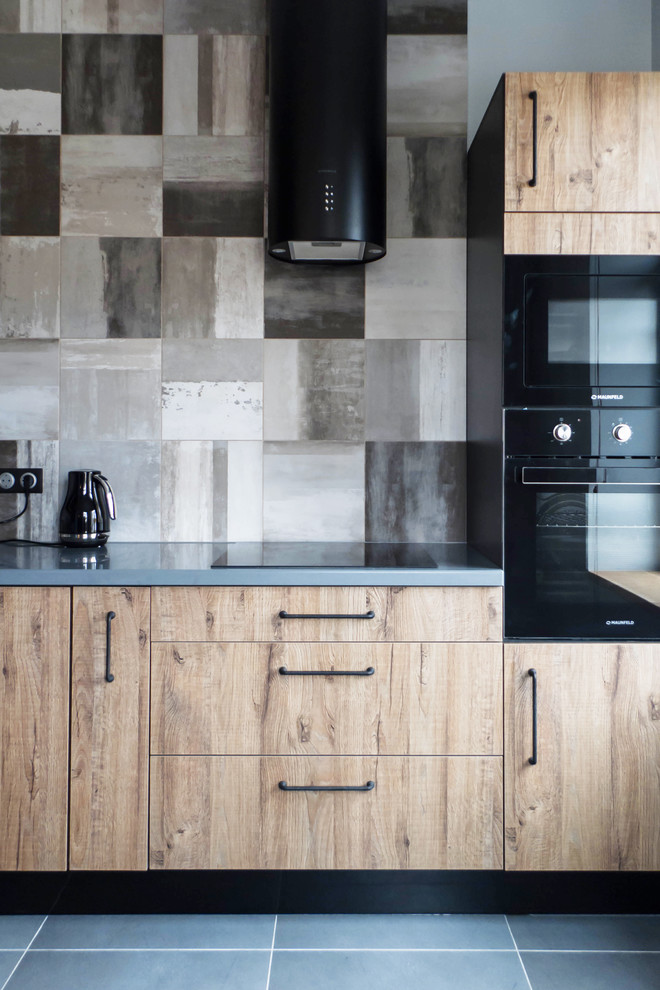 Cette photo montre une cuisine industrielle en bois clair avec un placard à porte plane, une crédence grise, un électroménager noir, un sol gris et un plan de travail gris.