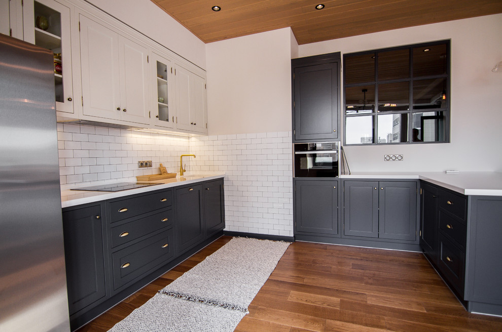 Photo of a medium sized traditional u-shaped kitchen/diner in Moscow with an integrated sink, shaker cabinets, black cabinets, composite countertops, white splashback, metro tiled splashback, stainless steel appliances, dark hardwood flooring, a breakfast bar, brown floors and white worktops.