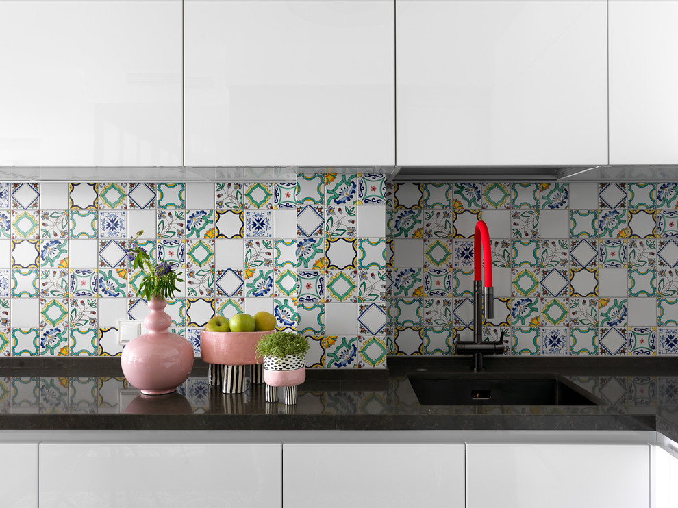 Cette photo montre une cuisine tendance avec un placard à porte plane, des portes de placard blanches, une crédence multicolore et plan de travail noir.