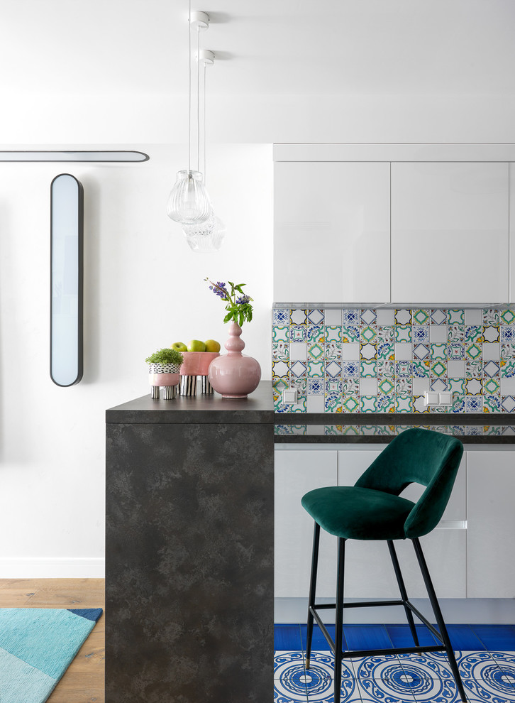 Idée de décoration pour une cuisine design avec un placard à porte plane, des portes de placard blanches, une crédence multicolore, un sol bleu et plan de travail noir.