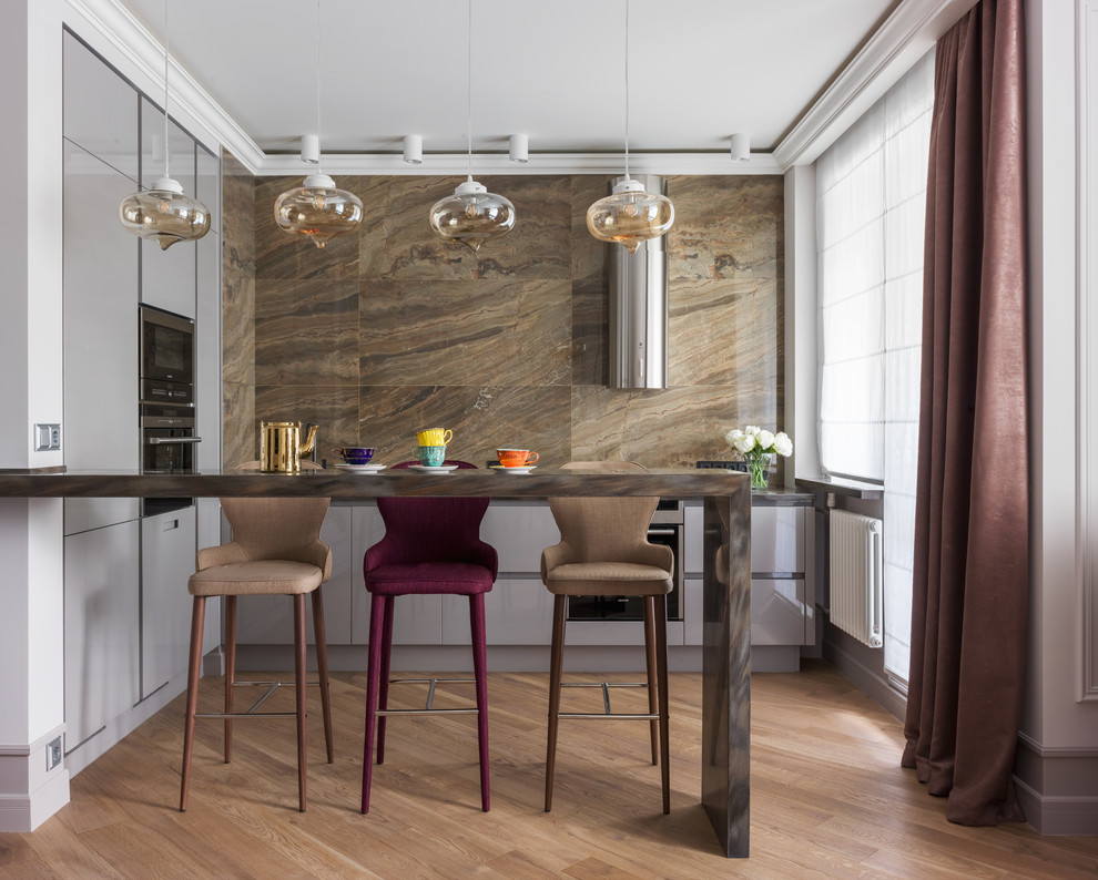 Cette image montre une cuisine ouverte traditionnelle en L avec un placard à porte plane, des portes de placard grises, une crédence marron, un électroménager en acier inoxydable, un sol en bois brun et un sol marron.