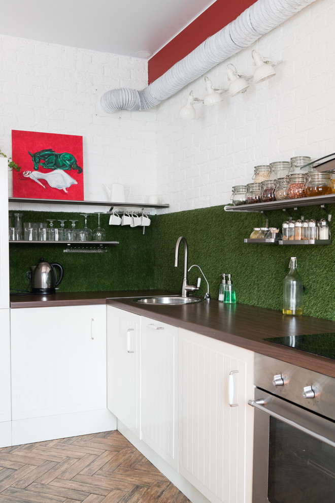 На фото: угловая кухня в скандинавском стиле с накладной мойкой, белыми фасадами, зеленым фартуком и техникой из нержавеющей стали без острова с