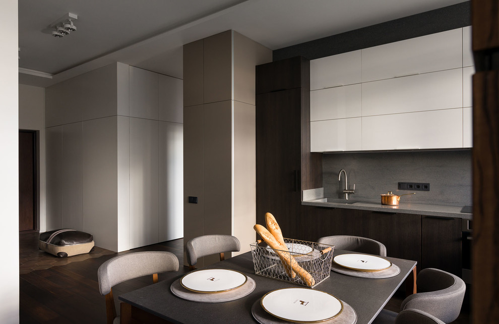 Стильный дизайн: кухня-гостиная в современном стиле с плоскими фасадами, темными деревянными фасадами и серым фартуком без острова - последний тренд
