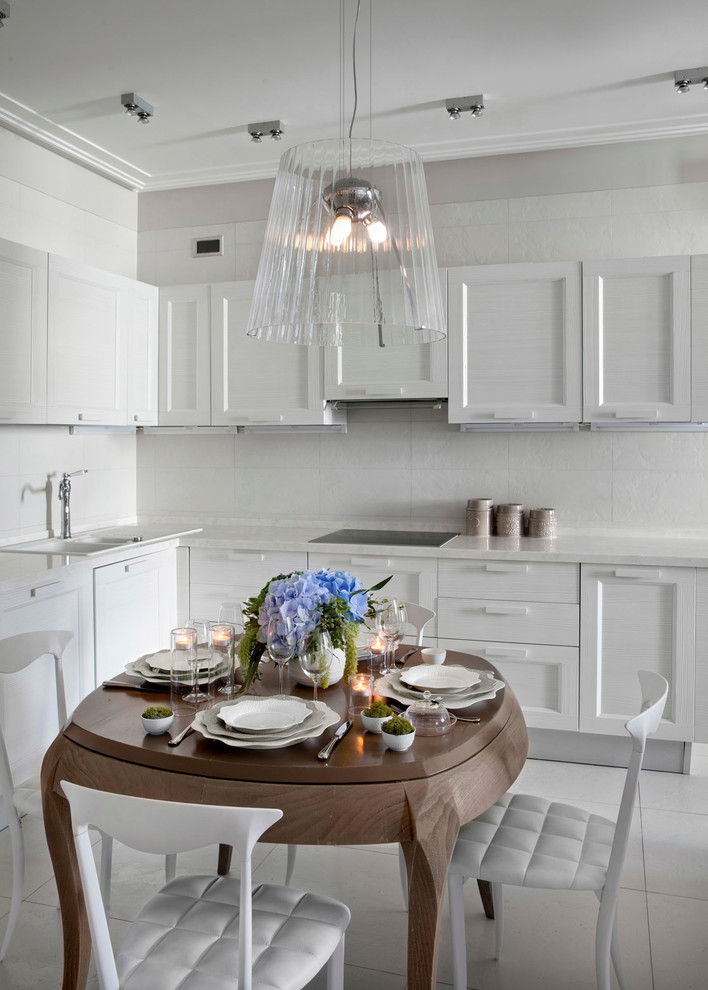 На фото: кухня в стиле неоклассика (современная классика) с накладной мойкой, белыми фасадами, белым фартуком, обеденным столом, фасадами в стиле шейкер и белой техникой с
