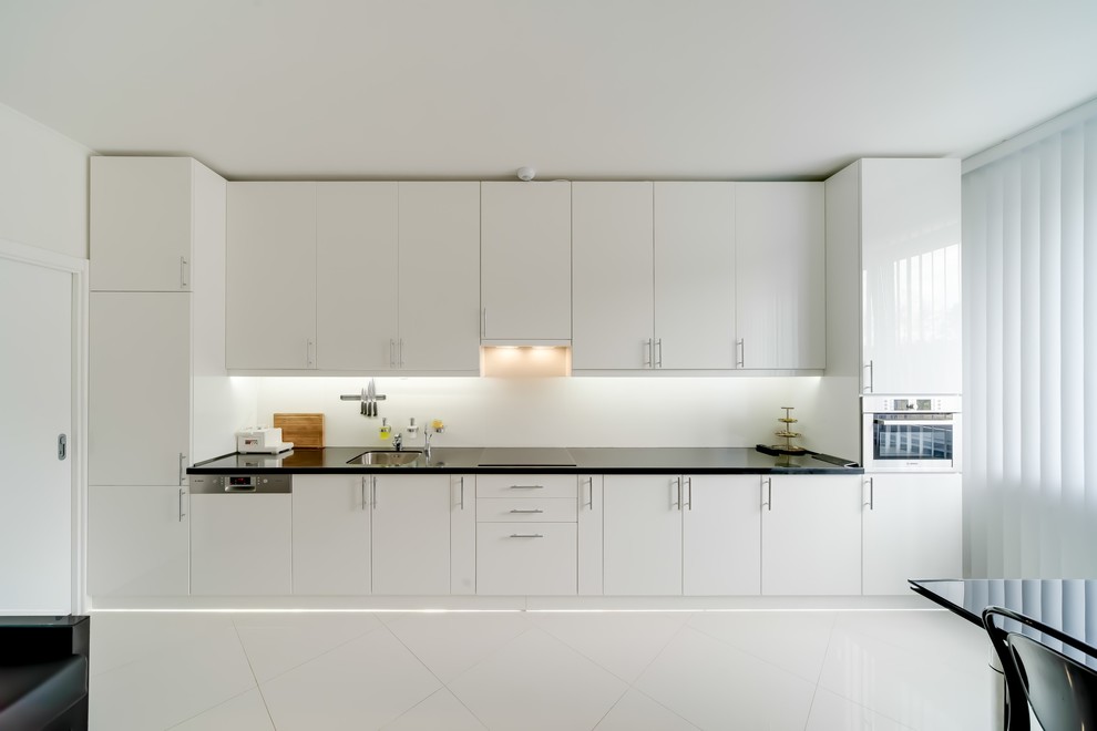 Diseño de cocina lineal contemporánea abierta sin isla con fregadero bajoencimera, armarios con paneles lisos, puertas de armario blancas, salpicadero blanco y suelo blanco