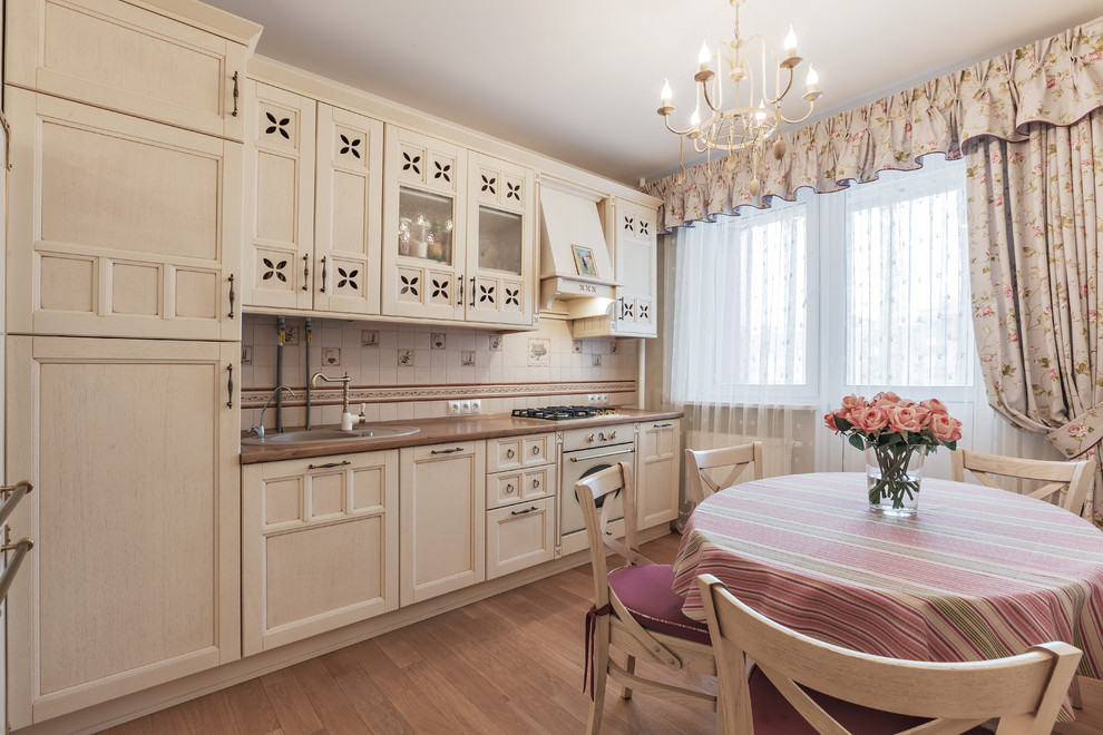Foto på ett shabby chic-inspirerat linjärt kök, med en nedsänkt diskho, luckor med infälld panel, beige skåp, beige stänkskydd, vita vitvaror och brunt golv