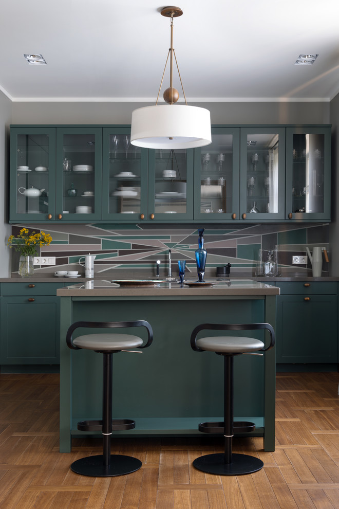 Modern inredning av ett grå grått parallellkök, med gröna skåp, flerfärgad stänkskydd, en köksö, brunt golv, luckor med glaspanel och mellanmörkt trägolv