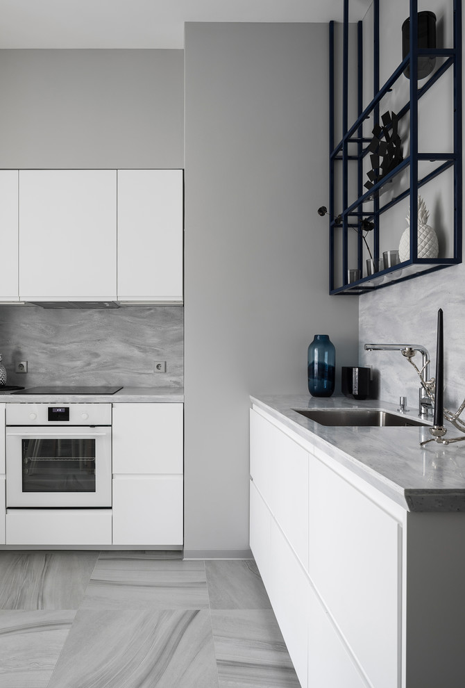 Réalisation d'une cuisine grise et blanche design en L avec un évier encastré, un placard à porte plane, des portes de placard blanches, une crédence grise, un électroménager blanc et un sol gris.