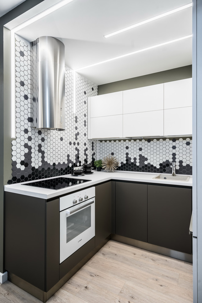 Inredning av ett modernt litet u-kök, med en nedsänkt diskho, släta luckor, flerfärgad stänkskydd, vita vitvaror, beiget golv, grå skåp, stänkskydd i mosaik och ljust trägolv