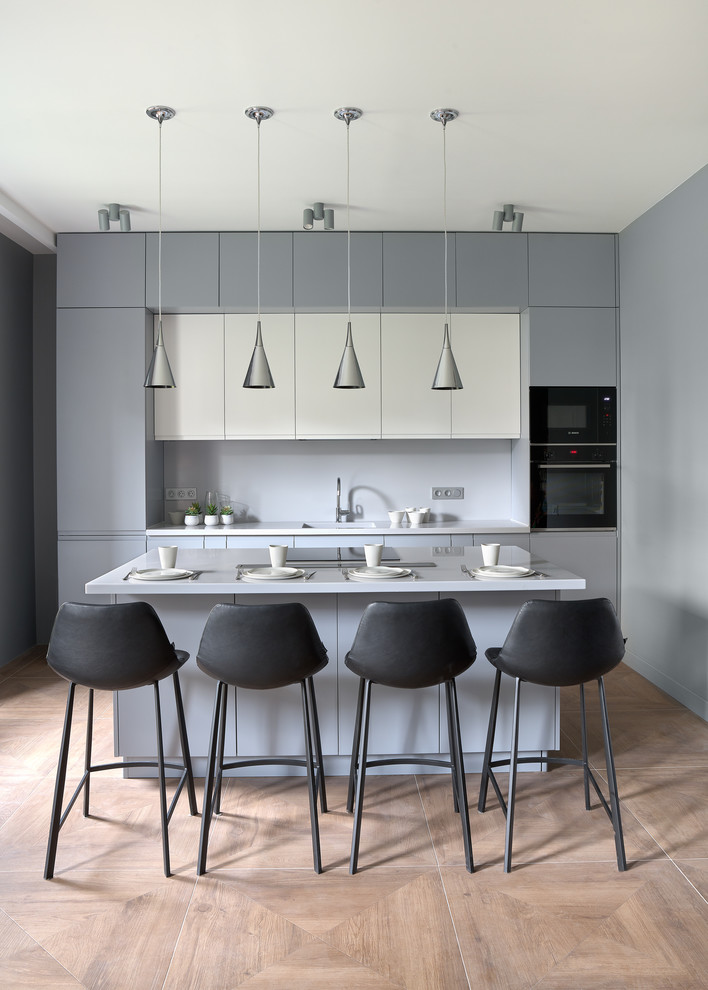 Idée de décoration pour une cuisine parallèle et grise et noire design avec un placard à porte plane, des portes de placard grises, îlot, un sol marron et un plan de travail gris.