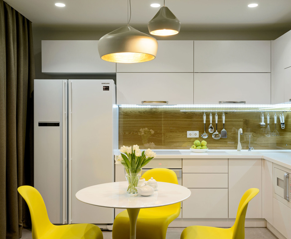 Свежая идея для дизайна: угловая кухня-гостиная в современном стиле с одинарной мойкой, плоскими фасадами, белыми фасадами, коричневым фартуком, белой техникой и серым полом без острова - отличное фото интерьера