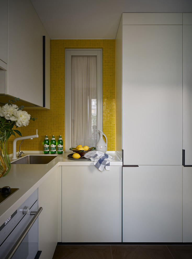 Eklektisk inredning av ett litet vit vitt kök, med en undermonterad diskho, släta luckor, vita skåp, bänkskiva i koppar, gult stänkskydd, stänkskydd i mosaik, vita vitvaror, klinkergolv i porslin och brunt golv