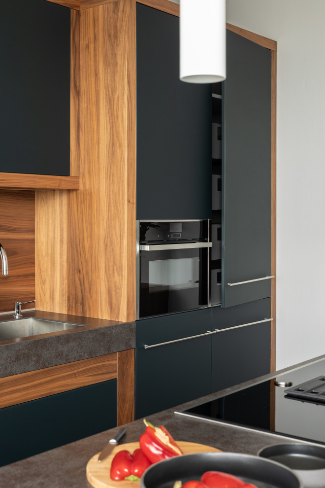Bild på ett mellanstort funkis grå linjärt grått kök och matrum, med en enkel diskho, luckor med glaspanel, svarta skåp, bänkskiva i kvartsit, brunt stänkskydd, stänkskydd i trä, integrerade vitvaror och en köksö