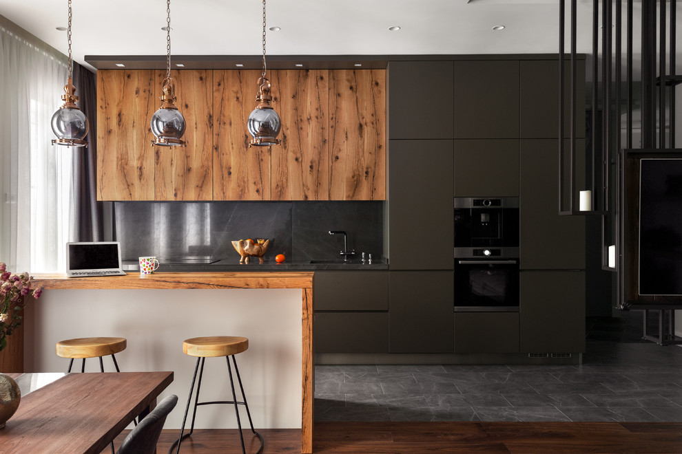 На фото: прямая кухня-гостиная в современном стиле с плоскими фасадами, черным фартуком, техникой из нержавеющей стали, островом, серым полом, серыми фасадами и деревянной столешницей с