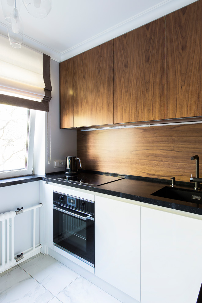 Foto på ett litet funkis svart kök, med en enkel diskho, släta luckor, vita skåp, bänkskiva i kvarts, brunt stänkskydd, stänkskydd i trä, svarta vitvaror, klinkergolv i porslin och vitt golv