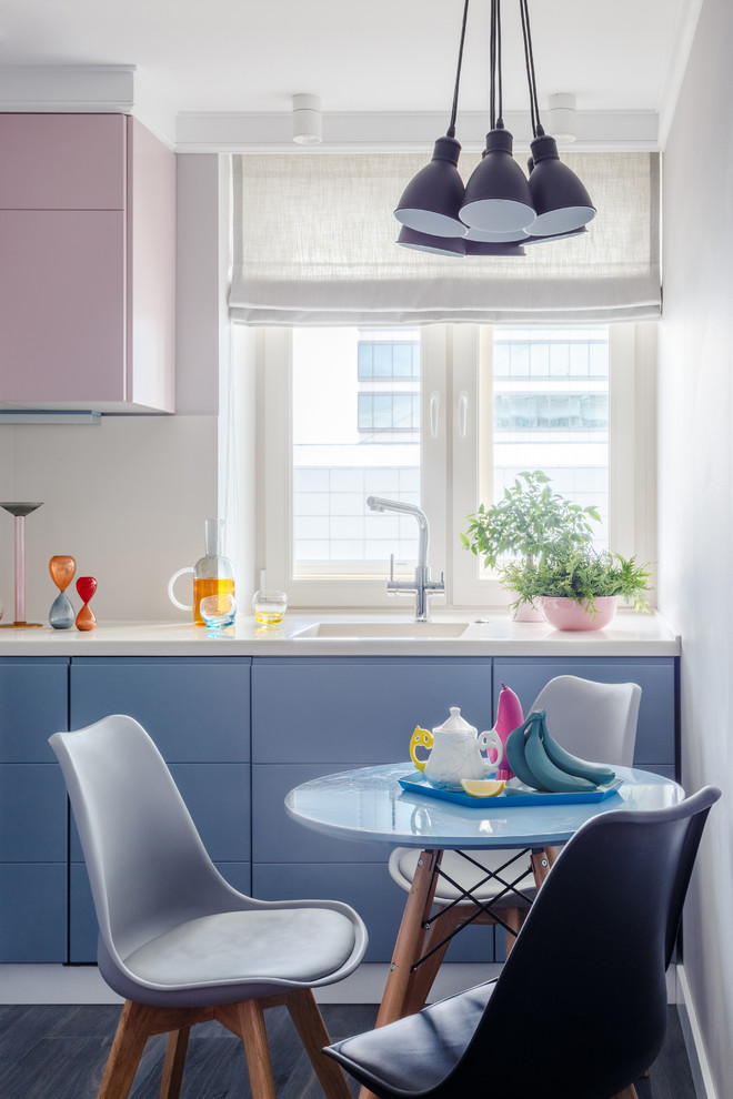 Minimalistisk inredning av ett avskilt, litet l-kök, med en integrerad diskho, släta luckor, blå skåp, bänkskiva i koppar, mörkt trägolv, grått golv, vitt stänkskydd och fönster som stänkskydd