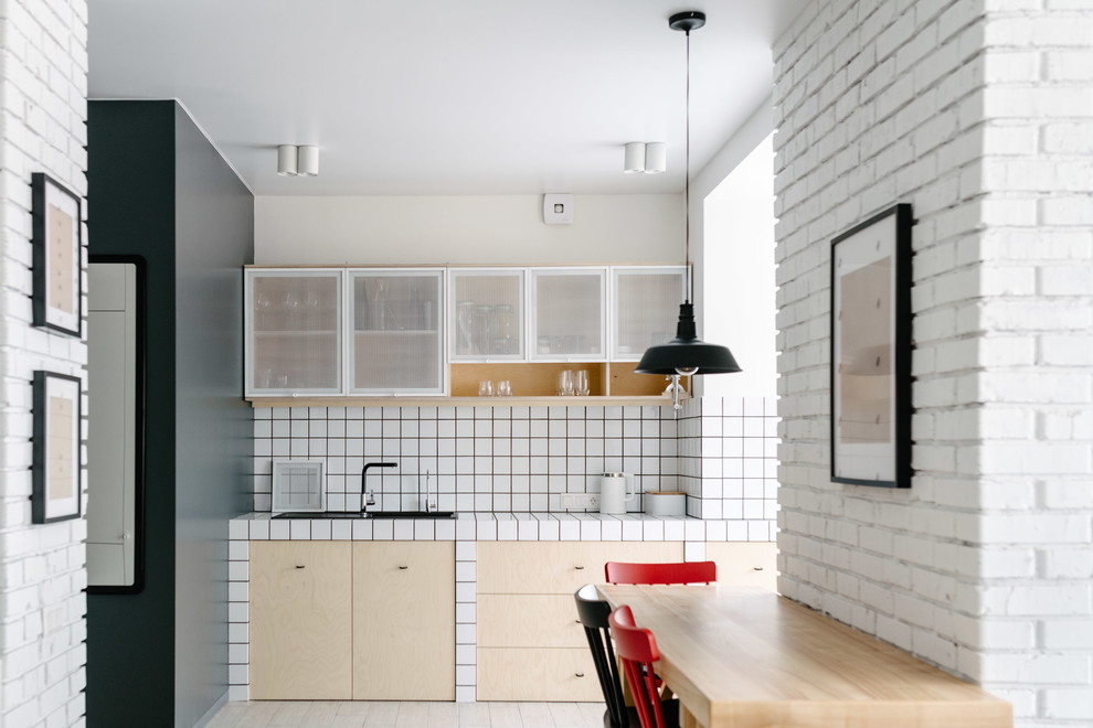 Modelo de cocina escandinava con fregadero encastrado, armarios con paneles lisos, puertas de armario de madera clara, encimera de azulejos, salpicadero blanco, suelo beige y encimeras blancas