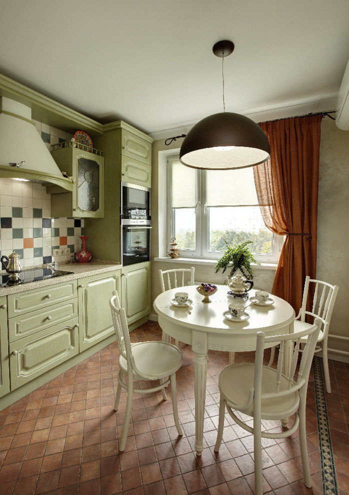 Aménagement d'une cuisine américaine classique avec aucun îlot, un placard avec porte à panneau surélevé, des portes de placards vertess, une crédence multicolore, un électroménager noir et tomettes au sol.