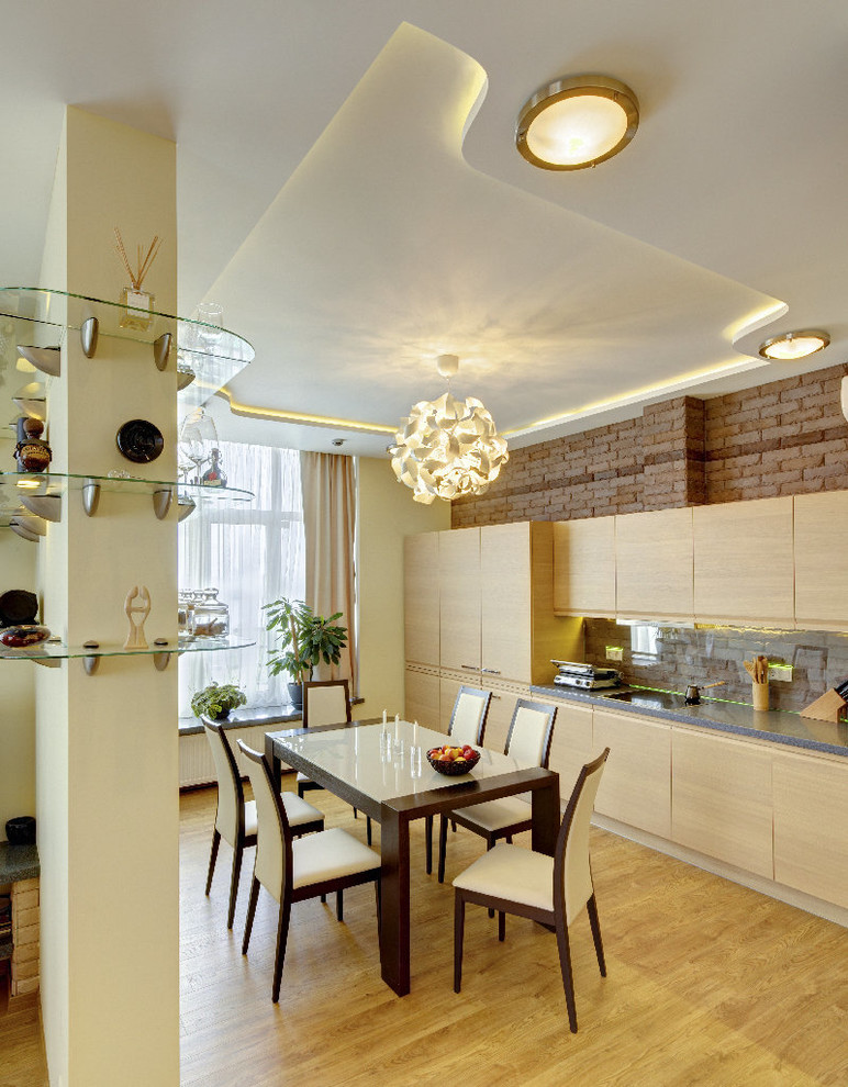 Свежая идея для дизайна: кухня-гостиная в современном стиле с плоскими фасадами, светлыми деревянными фасадами, коричневым фартуком и фартуком из стекла без острова - отличное фото интерьера