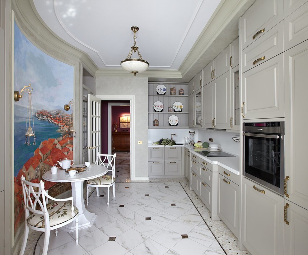 Klassisk inredning av ett avskilt l-kök, med grå skåp, vitt stänkskydd, rostfria vitvaror och marmorgolv