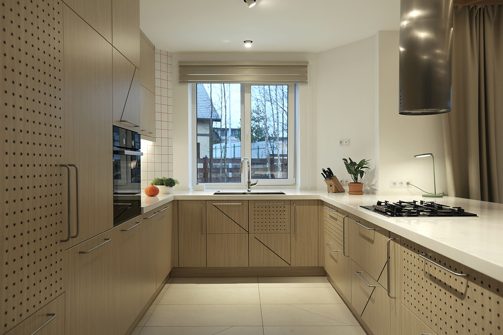 На фото: п-образная кухня-гостиная в скандинавском стиле с врезной мойкой, плоскими фасадами, светлыми деревянными фасадами, белым фартуком, черной техникой, полуостровом и белым полом с