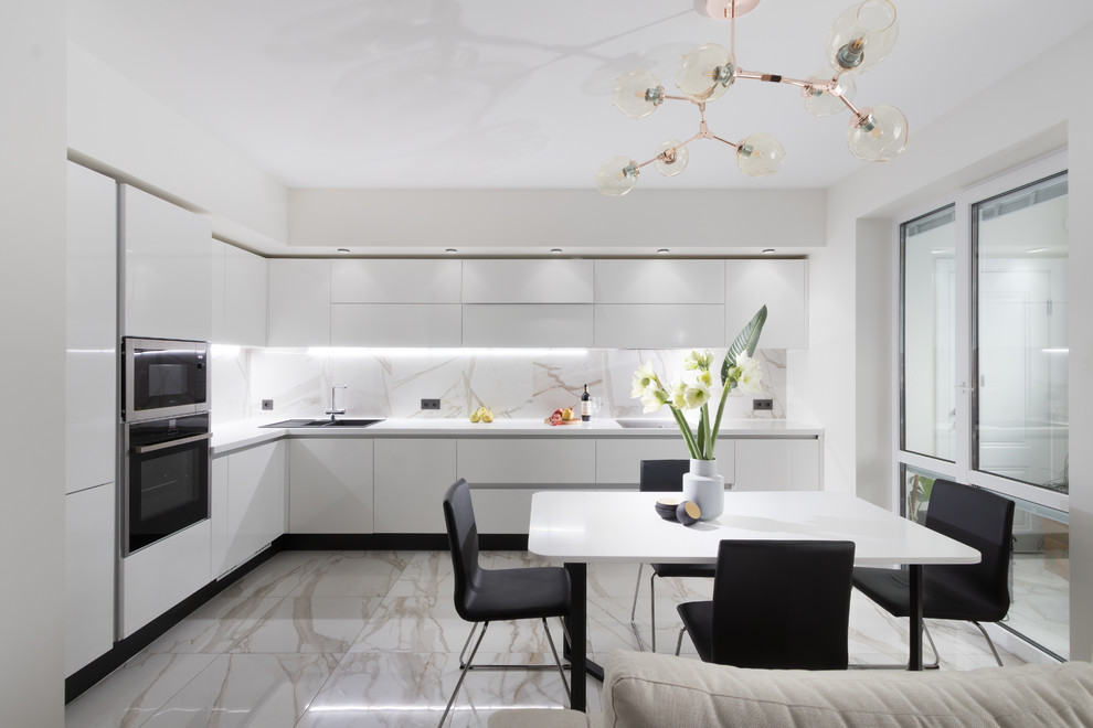 На фото: угловая кухня-гостиная в современном стиле с плоскими фасадами, техникой из нержавеющей стали, серым полом, белой столешницей и черно-белыми фасадами с
