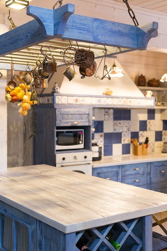 Immagine di una grande cucina rustica con lavello da incasso, ante con bugna sagomata, ante blu, top in legno, paraspruzzi blu, paraspruzzi con piastrelle in ceramica, elettrodomestici bianchi e pavimento in gres porcellanato