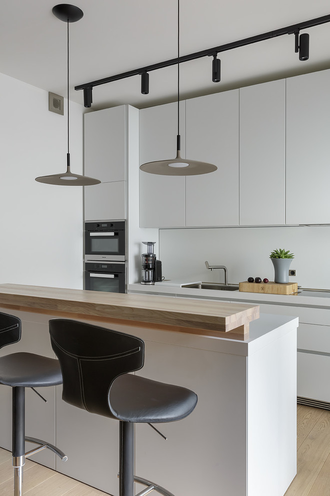 Идея дизайна: кухня среднего размера в современном стиле с обеденным столом, одинарной мойкой, белыми фасадами, белым фартуком, черной техникой, островом и бежевым полом