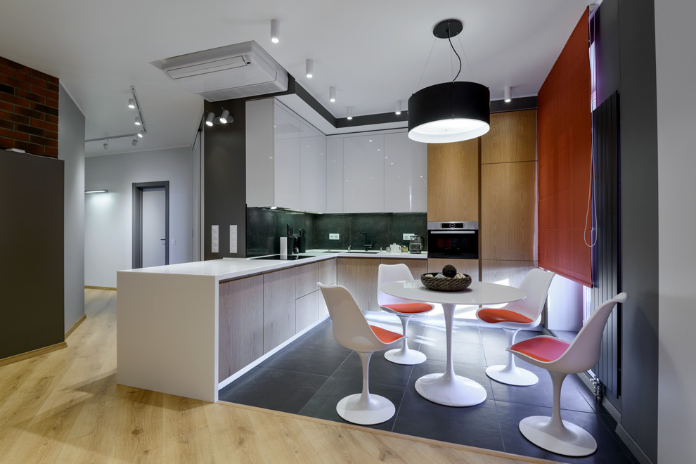 Пример оригинального дизайна: угловая кухня-гостиная в современном стиле с плоскими фасадами, техникой из нержавеющей стали и черным полом без острова