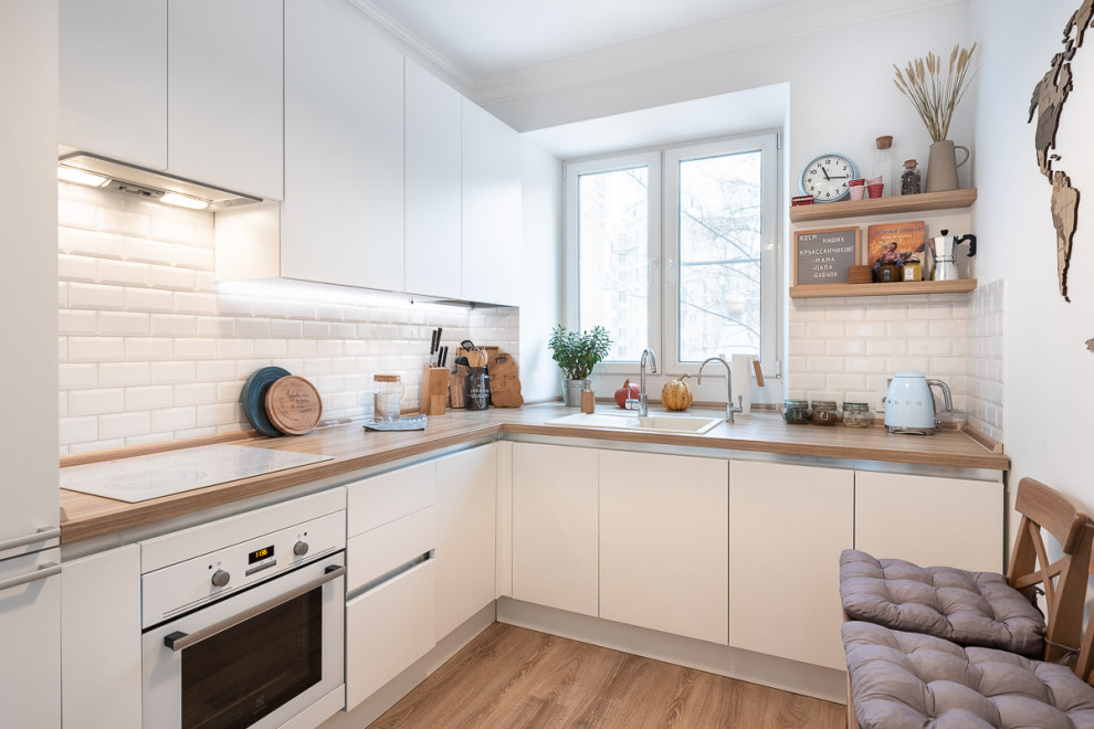 Bild på ett litet funkis beige beige l-kök, med en nedsänkt diskho, släta luckor, vita skåp, träbänkskiva, vitt stänkskydd, stänkskydd i porslinskakel, vita vitvaror och beiget golv