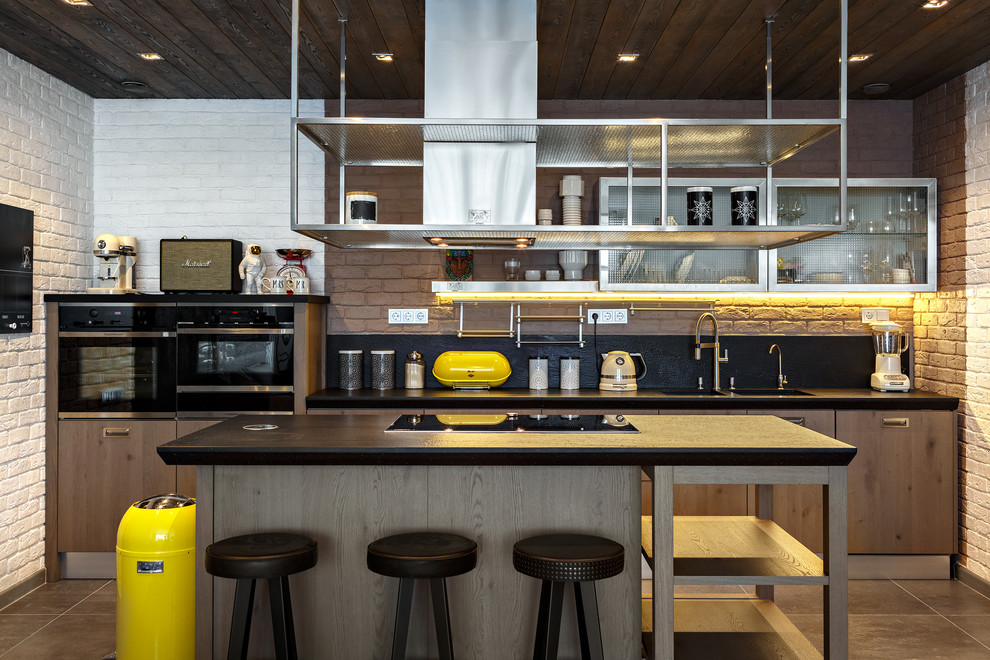 Идея дизайна: прямая кухня-гостиная в стиле лофт с плоскими фасадами, черным фартуком, черной техникой, островом, серым полом, двойной мойкой и фасадами цвета дерева среднего тона