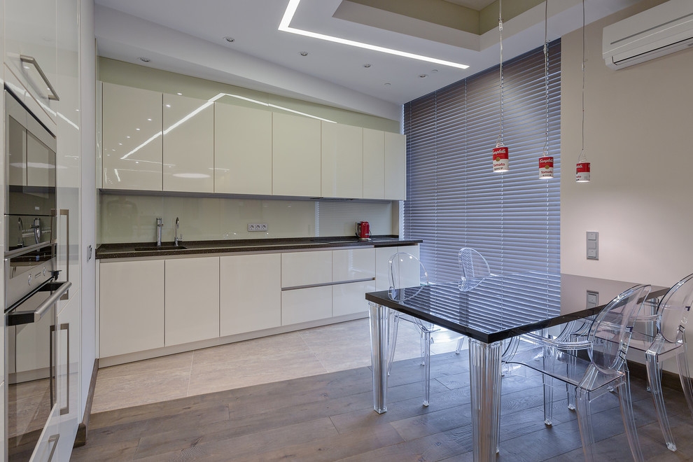 Photo of a contemporary l-shaped open plan kitchen in Moscow with flat-panel cabinets, white cabinets, white splashback, black appliances and no island.