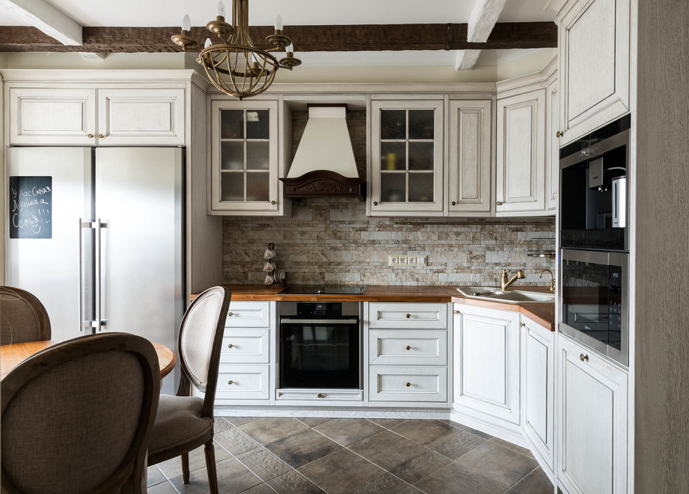 Foto di una cucina a L classica con lavello da incasso, ante con bugna sagomata, ante bianche, paraspruzzi beige e elettrodomestici neri