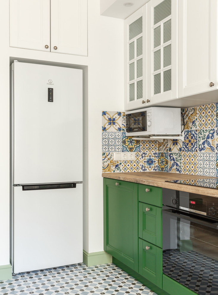 На фото: прямая кухня со шкафом над холодильником в скандинавском стиле с обеденным столом, фартуком из керамической плитки, фасадами с утопленной филенкой, зелеными фасадами, деревянной столешницей, разноцветным фартуком, черной техникой и коричневой столешницей