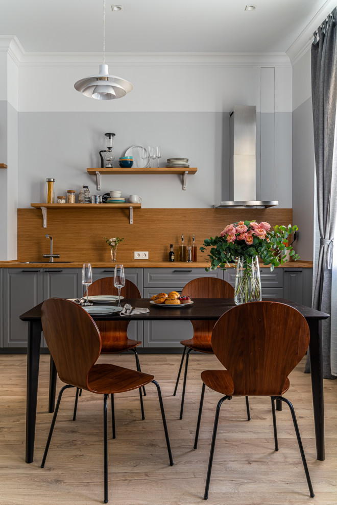 Inspiration for a medium sized scandi single-wall kitchen/diner in Saint Petersburg with a built-in sink, raised-panel cabinets, grey cabinets, wood worktops, brown splashback, wood splashback, black appliances, laminate floors, no island, brown floors and brown worktops.