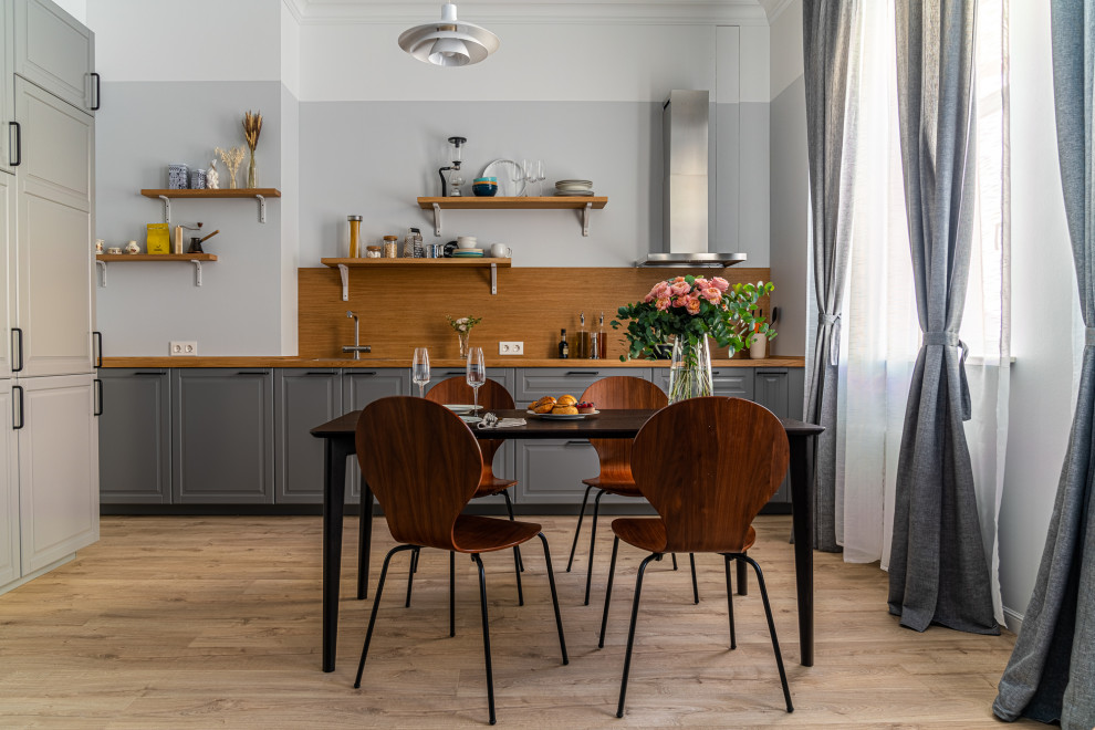 Example of a mid-sized danish single-wall laminate floor and brown floor eat-in kitchen design in Saint Petersburg with a drop-in sink, raised-panel cabinets, gray cabinets, wood countertops, brown backsplash, wood backsplash, black appliances, no island and brown countertops